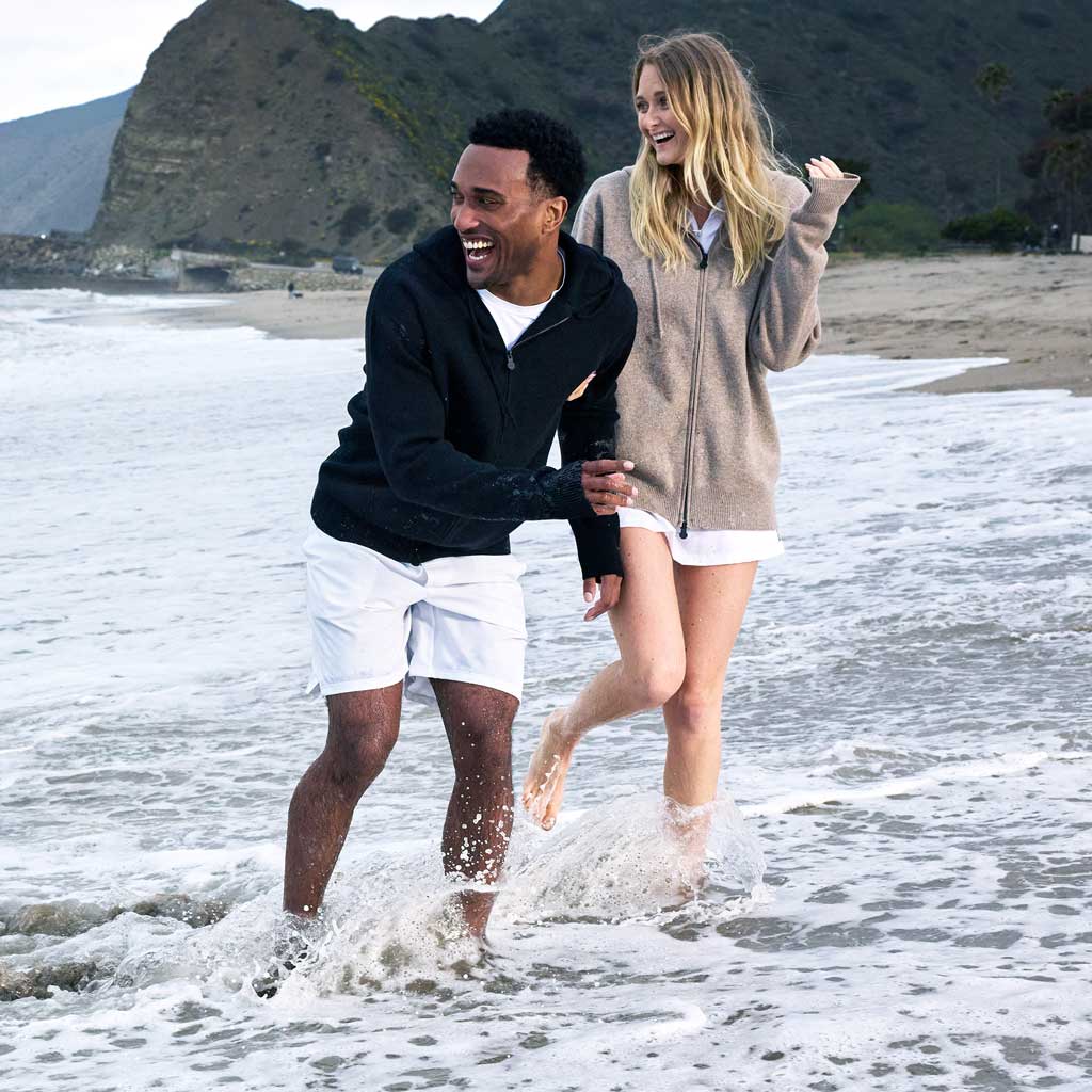 Two people walking on a beach with mountains in the background